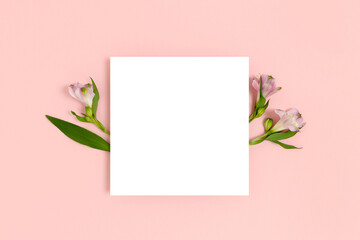 Composition with flowers and blank paper on a pink pastel background. Greetind card mockup.