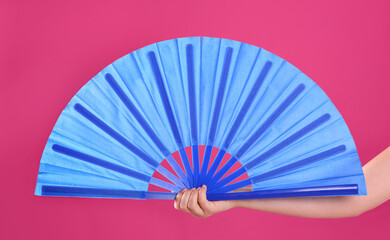 Woman holding blue hand fan on pink background, closeup