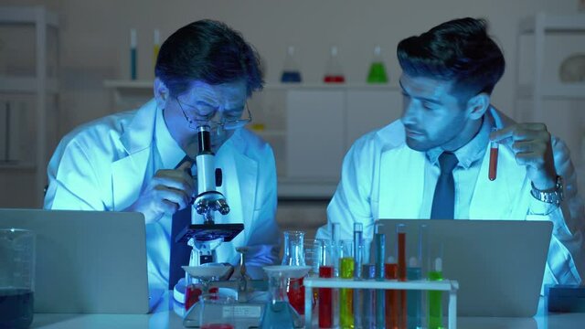 Asian scientists and caucasien scientists are looking into the microscope and recording the results.
