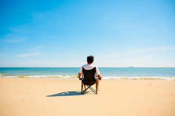 Man sitting on black chair on the beach with sea in background