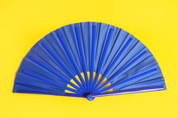 Blue hand fan on yellow background, top view