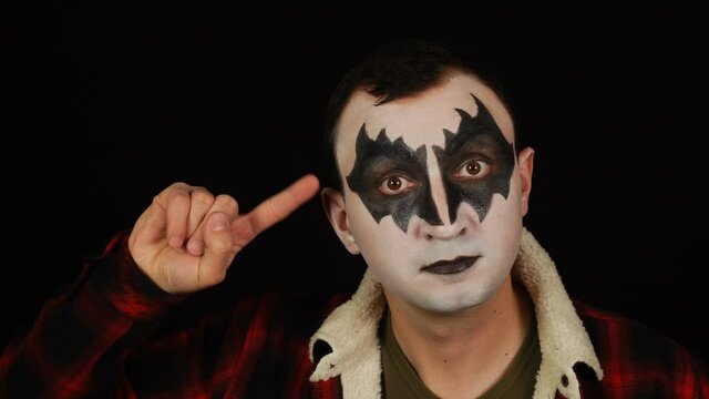 Man in demon makeup showing You are out of mind gesture on black background