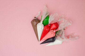 Multicolored glazing in icing bags on a pink background.  Set for decorating desserts.  Icing for...