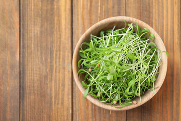 Bowl with fresh microgreen on wooden table, top view. Space for text