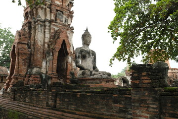 Side shot of old ruins buddha sit on beautiful pagoda background,grungy cement brick surrounding in Wat Mahathat in Ayutthaya province,Thailand.