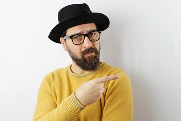 bearded man wearing hat and eyeglasses pointing aside worried and nervous with forefinger, concerned and surprise expression