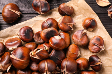 Tasty roasted edible chestnuts on black wooden table, top view