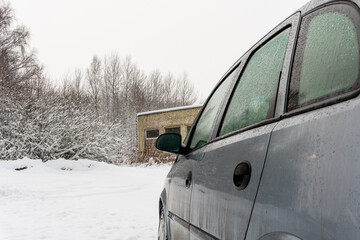 Dirty car on the background of an abandoned building and bushes on a snowy road, car breakdown on the road