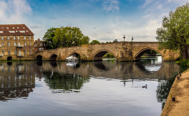 A boat passes through the old bridge at Riverside, Godmanchester that spans the River Great Ouse in springtime