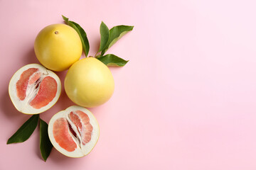 Fresh cut and whole pomelo fruits with leaves on pink background, flat lay. Space for text