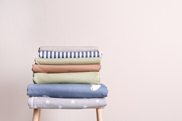 Plakat Stack of clean bed sheets on stool near beige wall. Space for text