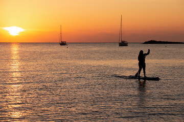 Man on stand up paddle board at sunset in calm waters with a sailboat