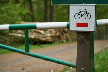 Rural road in the forest with closed green white barrier. Bike route sign on a path in a forest     
