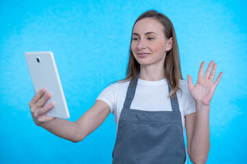 A woman smiles and waves a tablet webcam during a video call on a blue background