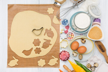 Easter cooking background with dough, eggs, rolling pin, whisk for whipping, cookie cutters, sugar sprinkling, flour. Rustic white wooden background, top view.