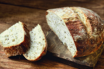 A loaf of fresh homemade bread and sliced pieces lie on a wooden table. Useful yeast-free baking with your own hands. Close-up.