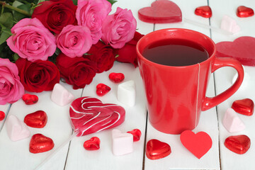 Fototapeta na wymiar Valentine's Day concept. Mug of tea, red and pink roses and lots of candy hearts - lollipops, chocolate and marshmallows.