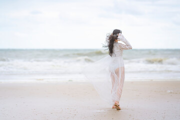 Fototapeta na wymiar Beautiful women in white dress happily strolling at the beach, beautiful woman dressed in white bride