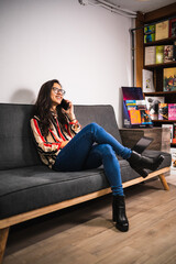 Young woman talks with phone while using laptop on sofa