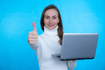 Portrait of an excited young girl holding laptop computer and celebrating success isolated over blue background