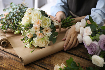 Florist wrapping beautiful wedding bouquet with paper at wooden table, closeup
