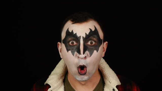 Man in demon makeup screaming in rage on black background