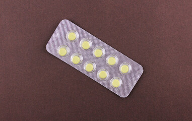 Blister pack of small yellow pills on brown background