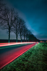 A country road with a moving car with shining red lights at night