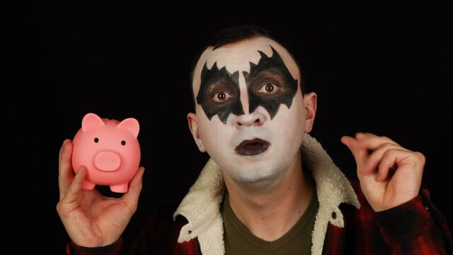 Man in scary mask putting a coin in piggy bank and saving money for halloween