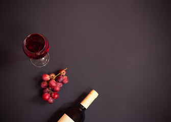 Glass of red wine, purple grape and bottle of red wine on dark background.
