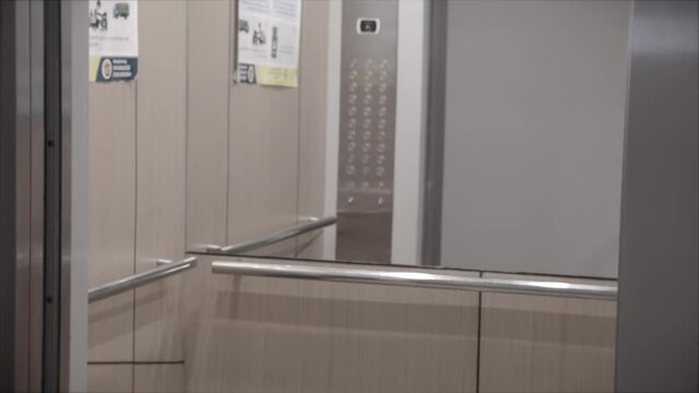 Opening the door is an elevator. Metal doors smoothly open and close. Silver new elevator on the 14st floor. The elevator doors open.