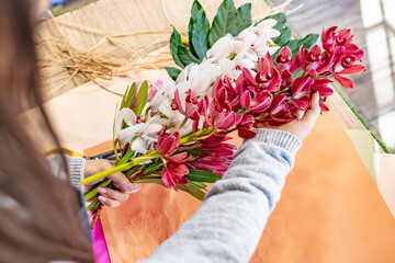Fototapeta na wymiar Cheerful young florist cutting flowers for bouquet at the counter . Close-up of unrecognizable florist wrapping beautiful bouquet in ribbon and striped paper at workplace