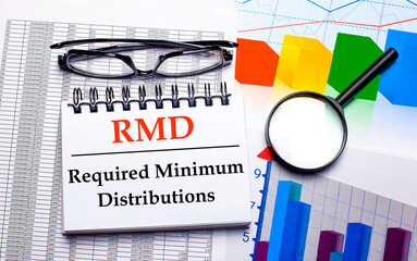 Glasses, magnifier, color charts and a white notepad with text RMD Required minimum Distributions on the desktop. Business concept. View from above