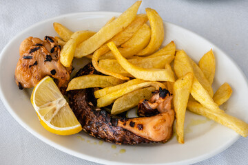 Grilled octopus served with lemon and fries. Traditional Greek dish.