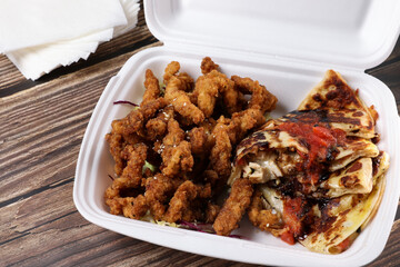 Top view of table fool of food in plastic containers. Food delivery. Chicken salad, chicken wings with sous, burger on french fries on a wooden table. Business lunch.
