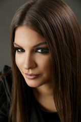 Studio portrait of brunette woman with straight long hair and glamorous smokey eyes makeup.
