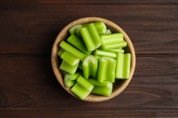 Cut celery in bowl on wooden table, top view