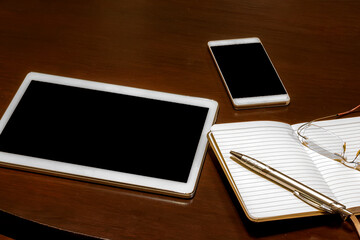 Office table: mobile phone, tablet, glasses, notebook and pen with copy space. Gadgets on a wooden table.