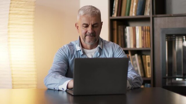 Mature man surfing internet on laptop computer, sitting at cabinet at home