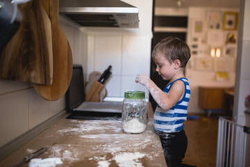 cute little boy playing with flour and making mess in kitchen