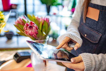 Young female florist using a digital tablet in her flower shop. Florist Woman Checking Her Personal Planer, Digital Tablet. Female florist using tablet computer in flower shop