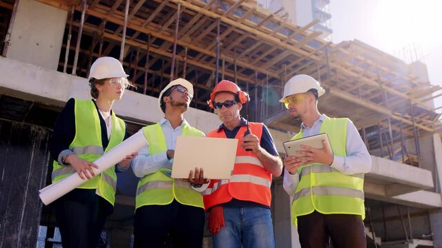 Mature foreman and his construction team engineers and architect using laptop and digital tablet to analyzing the plan of work foreman using ration to discussing with other group of specialists from