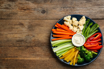 Plate with celery sticks, other vegetables and dip sauce on wooden table, top view. Space for text