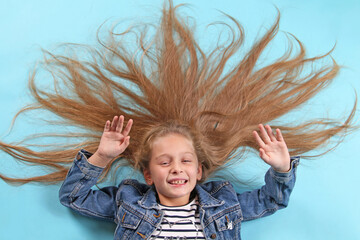 Portrait of a blonde girl dressed in a striped t-shirt and denim jacket lying on a blue background...