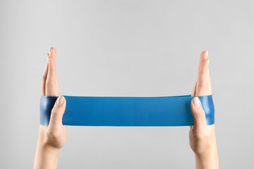 Woman with fitness elastic band on light grey background, closeup