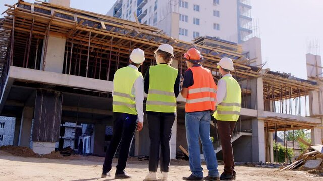 In a large construction site group of specialists and foreman together have a meeting they analyzing the future plan of work wearing protective equipment