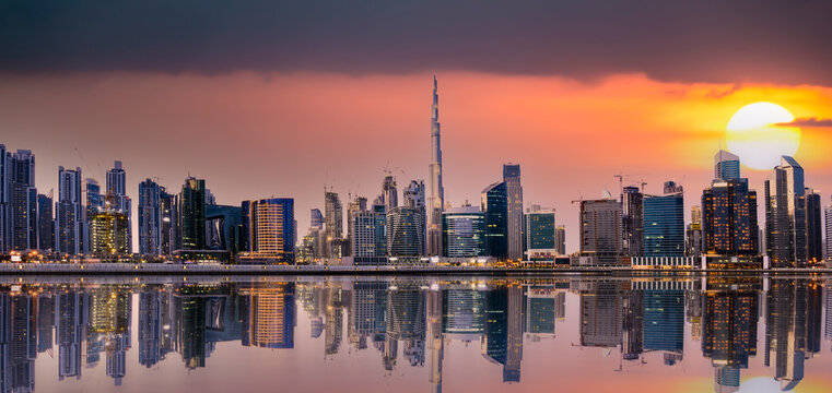 Panoramic view of the Dubai skyline at sunset with buildings and skyscrapers reflected on the river flowing in the foreground. Dubai, UAE.