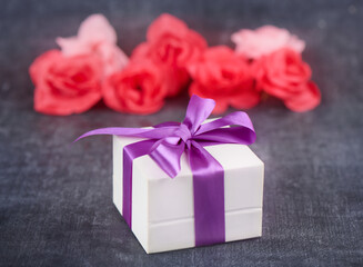 Gift box with purple ribbon and roses on gray background close up