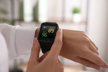 Woman measuring oxygen level with smartwatch indoors, closeup