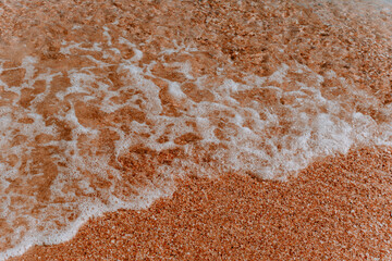 sea foam on the yellow sand. The texture of the sand closeup as background.Sea foam on the background of sand.Soft waves and sea foam on the sand with sunny highlights. Beautiful beach background